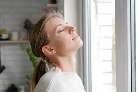 Femme détendue, les yeux fermés, près d'une fenêtre baignée de lumière