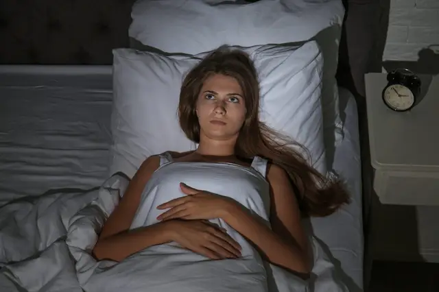 Femme éveillée dans son lit en pleine nuit, le regard tourné vers le plafond