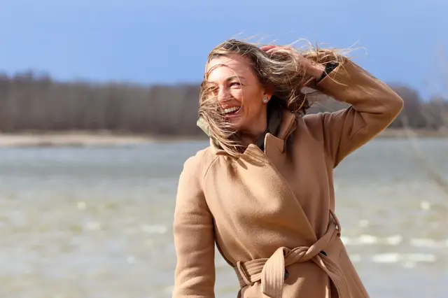 Femme souriante, cheveux au vent, au bord de l'eau