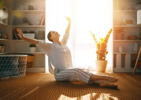 Femme qui s'étire au sol dans un salon baigné de soleil