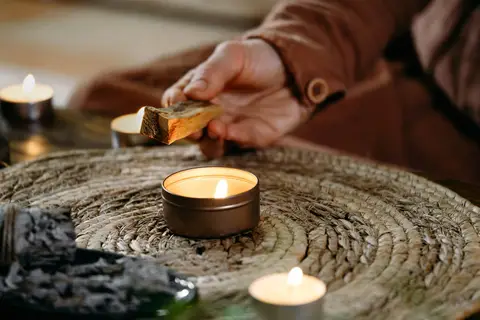 Main qui allume un bâton d'encens près de bougies, sur un set tressé