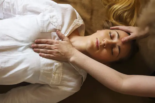 Femme allongée, yeux fermés, pendant qu'une praticienne pose les mains sur sa tête et son épaule